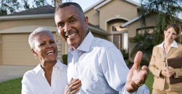 elderly couple standing in front of realtor and house