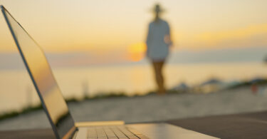 woman walking on beach with computer in foreground