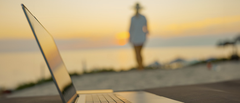 woman walking on beach with computer in foreground